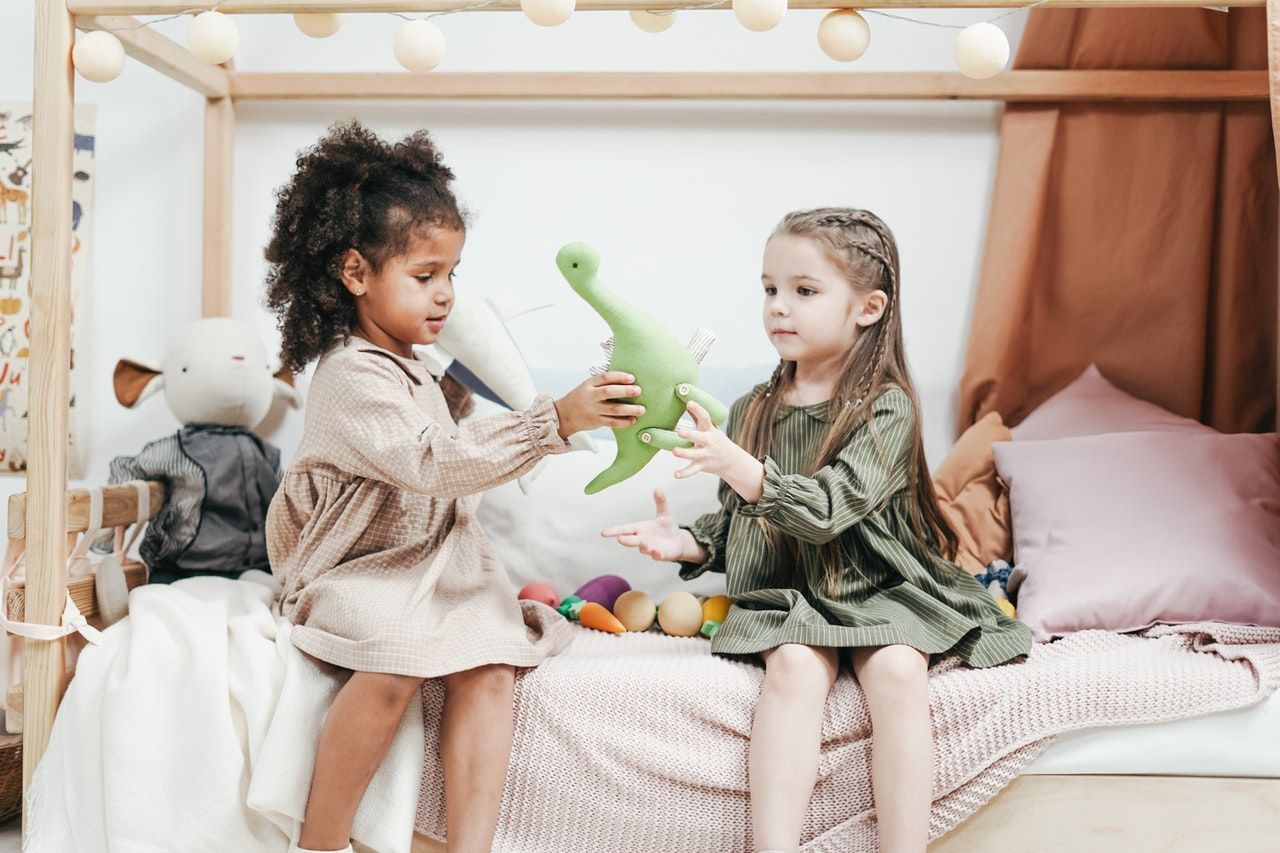 Image of two girls sharing a dinosaur toy